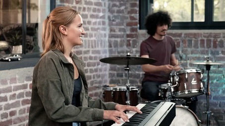 young woman playing a digital piano along with a drummer